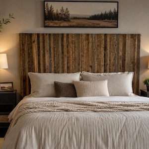May include: A bedroom scene featuring a tall headboard constructed from vertical reclaimed wood planks. The bed is dressed in light beige linens with a chunky knit throw blanket, two large pillows, and a smaller dark brown textured accent pillow.