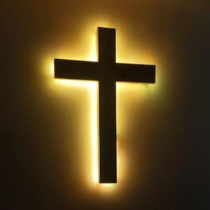 Peut inclure: Une croix en bois sombre avec une lumière chaude et brillante émanant de derrière. La croix est fixée sur un mur de couleur neutre, créant un contraste saisissant entre la silhouette sombre et le fond éclairé.