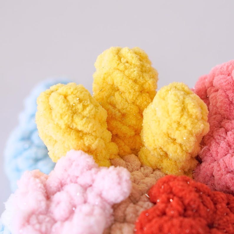 May include: Close-up of a colorful crocheted flower with yellow, pink, and red yarn. The flower is made with a fluffy, textured yarn.