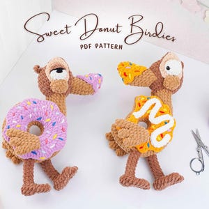 Puede incluir: Dos figuras de pájaros de ganchillo hechas a mano, cada una con un cuerpo de rosquilla. Un pájaro tiene una rosquilla morada con chispas de colores, el otro tiene una rosquilla amarilla con glaseado blanco. El texto "Sweet Donut Birdies PDF Pattern" está en la parte superior.