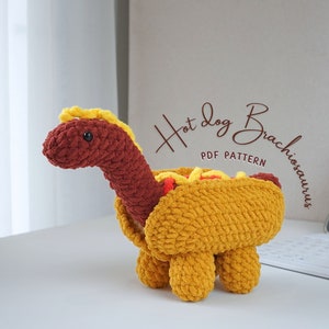 May include: Crocheted hot dog dinosaur toy with a mustard and ketchup topping. The toy is brown, yellow, and red. The text "Hot Dog Brachiosaurus PDF Pattern" is written in brown on a white background.