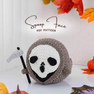 Op de afbeelding: Een gehaakte Halloween-thema knuffel in de vorm van een Grim Reaper met een schedelgezicht. De knuffel is grijs en wit, met een kleine zeis. De tekst "Spoop Face PDF Pattern" staat bovenaan.