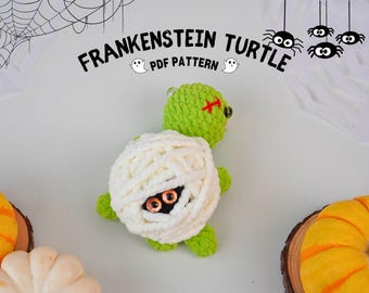 May include: A green crocheted Frankenstein turtle with white yarn wrapped around its shell. The turtle has red stitches for a scar and black eyes. The background is white with a black spider web and black spiders.