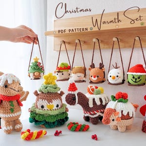 May include: A set of crocheted Christmas ornaments, including a gingerbread person, a Christmas tree, a snowman, a reindeer, an elf, and a pudding. The ornaments are hanging on a wooden shelf with the text "Christmas Warmth Set PDF Pattern" above them.