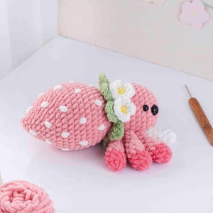 May include: A handmade pink crochet octopus with white polka dots, resembling a strawberry. It features white and yellow flower accents and black eyes. The tentacles are a gradient of pink and white.