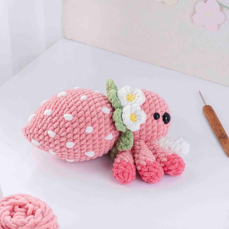 May include: A handmade pink crochet octopus with white polka dots, resembling a strawberry. It features white and yellow flower accents and black eyes. The tentacles are a gradient of pink and white.