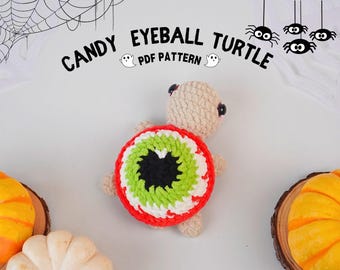 May include: A crocheted amigurumi toy turtle with a large green, white, and red eyeball on its shell. The turtle is beige and has black eyes. The background is white with a black spider web and black spiders hanging from the top.