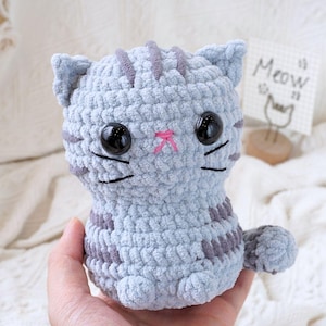 May include: A crocheted grey and white striped cat plush toy with black eyes and a pink nose.