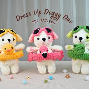 Pode incluir: Três brinquedos de cão de crochê, cada um com um acessório único. Um cão usa óculos amarelos e segura um pato amarelo. Outro usa óculos rosa e segura um flamingo rosa. O terceiro cão usa óculos verdes e segura um sapo verde. O texto diz "Dress-Up Doggy Duo PDF Pattern."