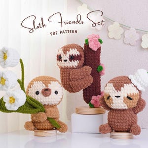 May include: A set of three crocheted sloth figures. One holds white flowers, another clings to a brown tree branch with pink flowers, and the third wears a white hat. The text "Sloth Friends Set PDF Pattern" is at the top.