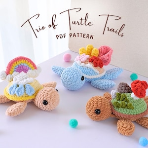 May include: Three crocheted turtle toys with different colored shells and designs. The first turtle has a rainbow shell, the second has a blue shell with a colorful flower design, and the third has a brown shell with a green and red mushroom design. The image includes the text "Trio of Turtle Trails PDF Pattern".