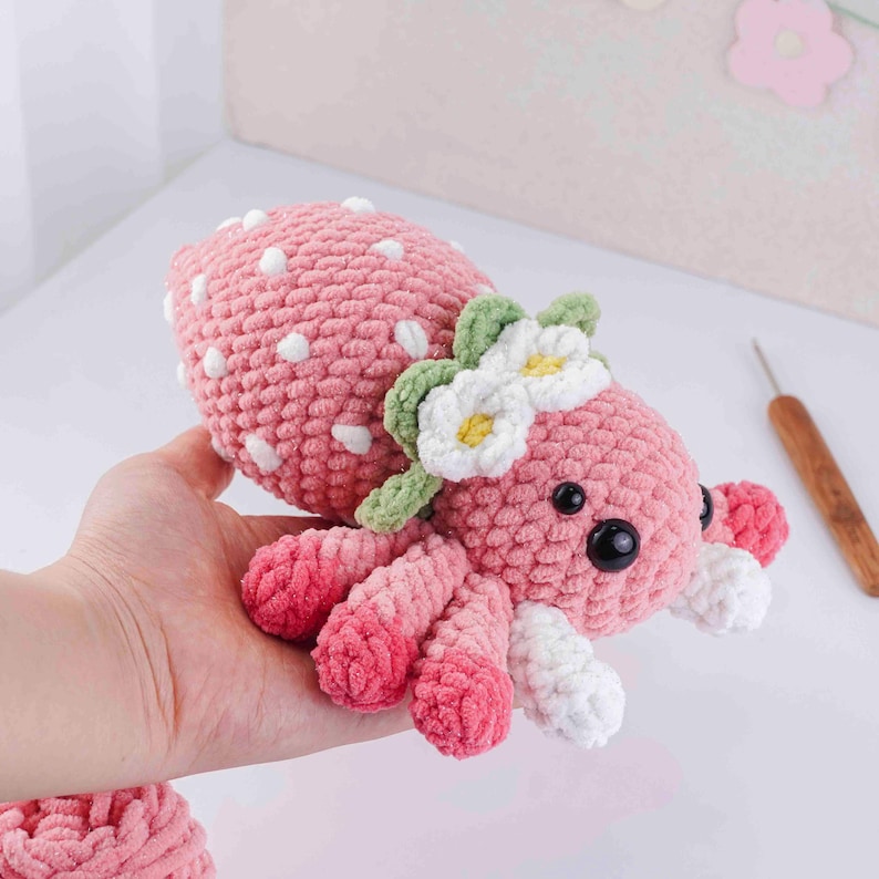 May include: A handmade pink crocheted octopus toy with white polka dots and a flower crown. The octopus has eight tentacles, black eyes, and is held in a hand. The toy is a soft, plush item.