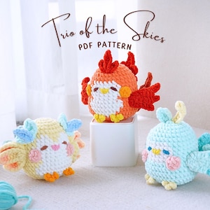 Puede incluir: Tres juguetes de pájaros amigurumi de crochet. Un pájaro rojo y naranja con un pico amarillo, un pájaro azul claro con un pico amarillo y un pájaro amarillo con un pico rosa. Los pájaros están sentados sobre una superficie blanca. Trio of the Skies PDF Pattern.