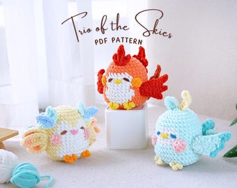 May include: Three crocheted amigurumi bird toys. A red and orange bird with a yellow beak, a light blue bird with a yellow beak, and a yellow bird with a pink beak. The birds are sitting on a white surface. Trio of the Skies PDF Pattern.