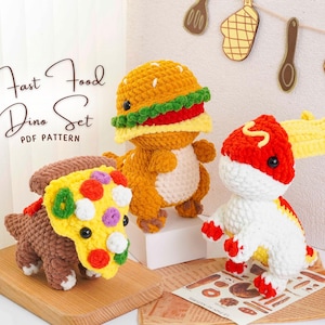 May include: A handmade crochet "Fast Food Dino Set" featuring three dinosaur figures. One is a burger, another a pizza slice, and the third a hot dog. The set is displayed on a wooden board and a printed paper with the text "Fast Food Dino Set PDF Pattern".
