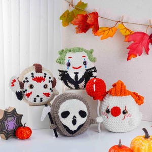 May include: A collection of handmade crochet Halloween characters, including Jason Voorhees, the Joker, a Grim Reaper, and a clown. Each character is round and features detailed facial expressions and accessories. Decorative fall leaves hang in the background.
