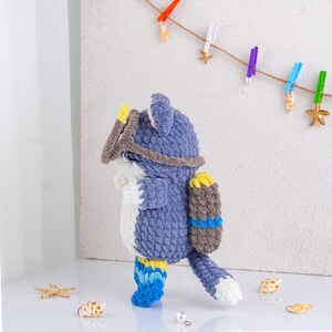 May include: A handmade blue and white crochet fox wearing a diving mask, snorkel, and scuba tank. The fox has blue and yellow flippers. Decorative seashells and starfish are scattered around the fox.
