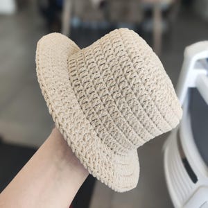 Op de afbeelding: Een beige gebreide bucket hat met een brede rand.
