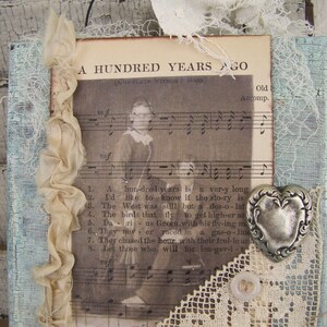 May include: A vintage-style, framed print with a musical score and lyrics for the song "A Hundred Years Ago". The print is decorated with lace, ribbon, and a silver heart charm. The text on the print reads "A Hundred Years Ago (Complete Without Bass)" and "Old Accomp."