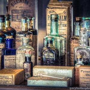 May include: A collection of vintage apothecary bottles with labels and stoppers. The bottles are filled with various liquids and are arranged on a shelf. Some of the labels include "Dr. Squills", "Gelsemium", "R.H.C.E. Dr. Pierce's Golden Medical Discovery", "S.B. Goff's Magic Oil Liniment", and "Pyramid Ointment".