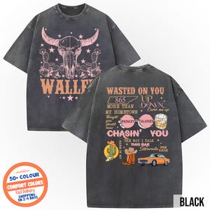 May include: Black graphic t-shirt with a steer skull and cactus design on the front. The back of the shirt features text and illustrations including a cowboy hat, car, and whiskey glasses. The shirt is a comfort color.