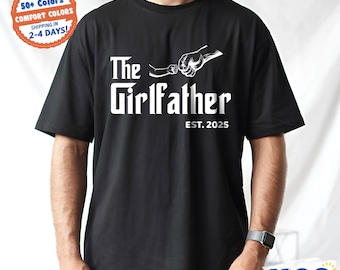 May include: Black t-shirt with the text "The Girlfather EST. 2025" in white. The design includes a graphic of two hands fist-bumping. The shirt is available in 50+ colors and made with comfort colors.