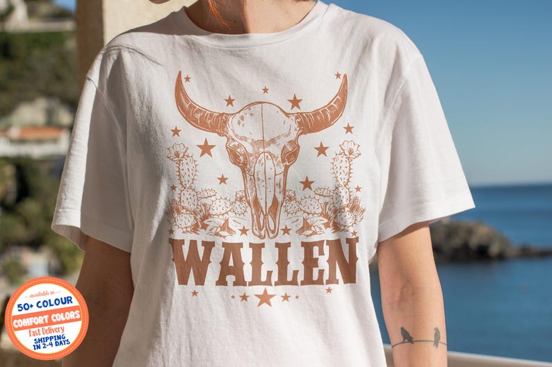 Pu&ograve; includere: T-shirt bianca con un design a teschio di bue marrone e la scritta "WALLEN" in un font in stile western. Il design include stelle e illustrazioni di cactus. Una t-shirt casual e confortevole.