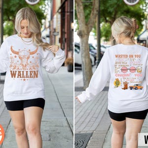 Pu&ograve; includere: Felpa bianca a maniche lunghe con grafica di teschio di bue e il nome "WALLEN" in marrone. La parte posteriore della maglietta presenta testo e grafica, tra cui "WASTED ON YOU" e "CHASIN' YOU".