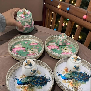May include: Decorative serving trays and jars with intricate designs. The trays have silver rims and feature floral and peacock motifs. The jars have lids with crystal knobs and painted floral patterns in shades of green, pink, and white.