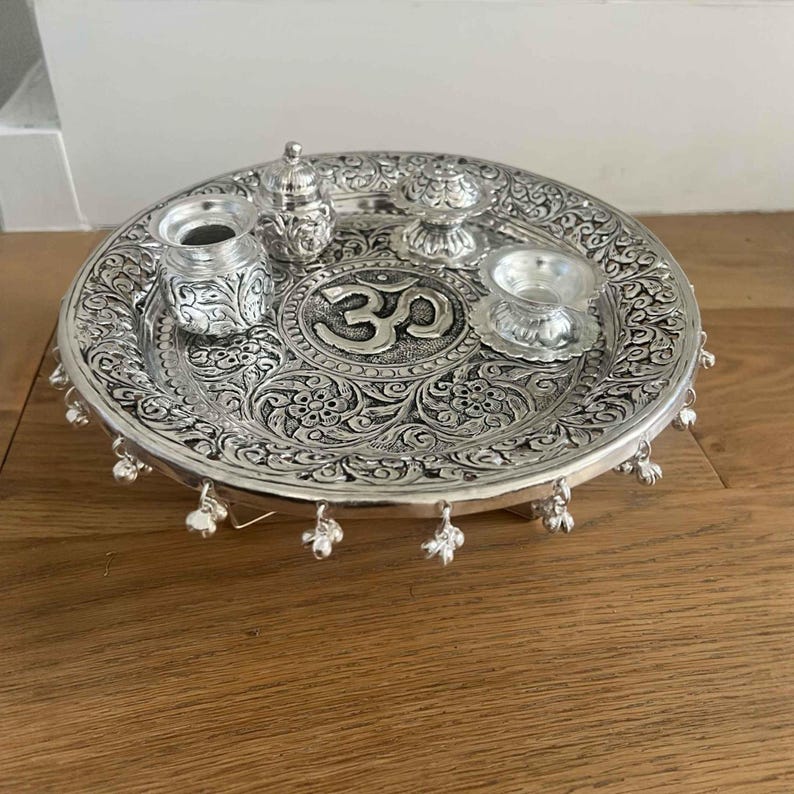 Macro shot of hand-engraved detailing on an antique German silver-plated brass pooja set showing the premium artisan finish.