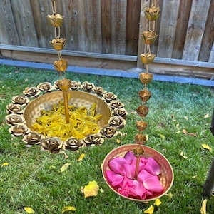 May include: Two decorative brass hanging bowls with flower petal accents. One bowl is filled with yellow petals, the other with pink petals. The bowls are suspended by chains of brass flower-shaped links, creating a unique garden ornament.
