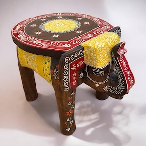 May include: Hand-painted wooden elephant stool with a round top. The elephant is painted in shades of brown, red, yellow, and green with intricate floral designs. The stool is a unique and decorative piece of furniture.