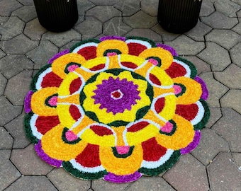 May include: A circular rug featuring a vibrant mandala pattern with concentric layers of purple, yellow, red, and green. The design consists of a central purple star-like shape surrounded by yellow petals, red arcs, and green borders with white accents.