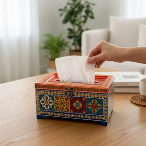 May include: A rectangular wooden tissue box holder featuring a vibrant, multi-colored floral pattern in shades of red, yellow, blue, and green. The box has a hinged lid with a metal latch and a central opening from which a white tissue is pulled.