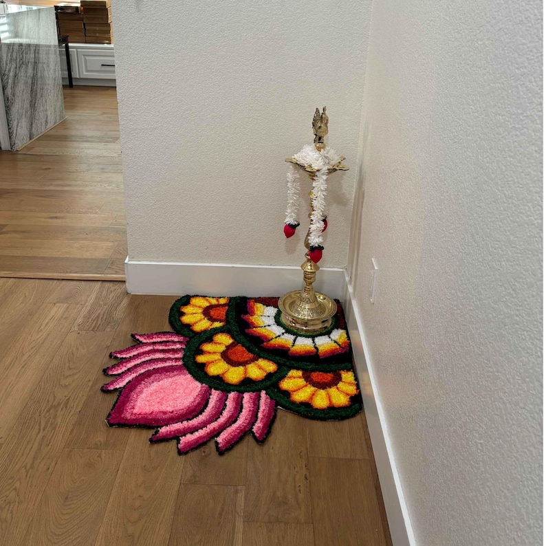 Indoor shot of a corner decorated with layered rangoli mats in warm yellow, orange, and pink hues, placed beside a brass lamp holder