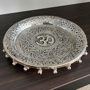 Top-down view of a 10.75-inch hand-engraved silver pooja thali with a detailed Om design and traditional floral border patterns.