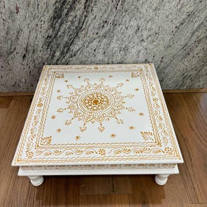 May include: White square table with four legs and a gold mandala design on the top.