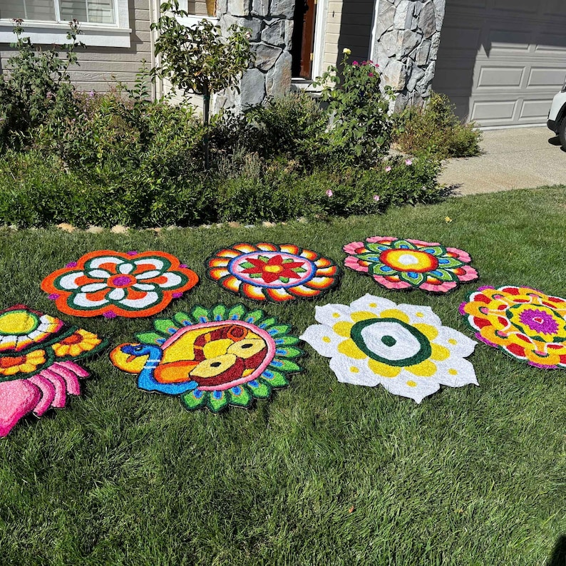 Seven round 3 ft rangoli mats laid out on grass, each with bright, multicolored floral and geometric designs for festive pooja decor