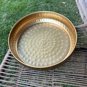 May include: A gold metal tray with a hammered texture. The tray is round and has a smooth, shiny finish.