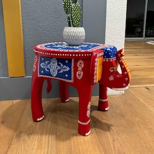 May include: A red wooden elephant stool with blue and white painted designs. The stool has a round top and four legs.