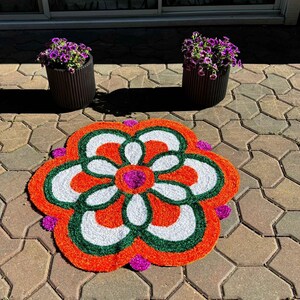 Close-up of a single red-and-white floral rangoli mat on a paved courtyard, showcasing a symmetrical petal pattern