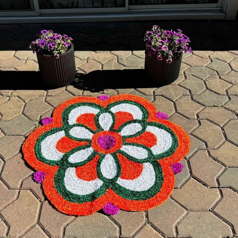Close-up of a single red-and-white floral rangoli mat on a paved courtyard, showcasing a symmetrical petal pattern