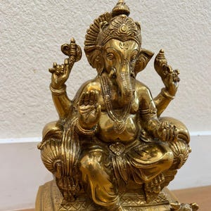 Seated Brass Ganesha statue on wooden base against white wall — ideal for pooja room or mantle