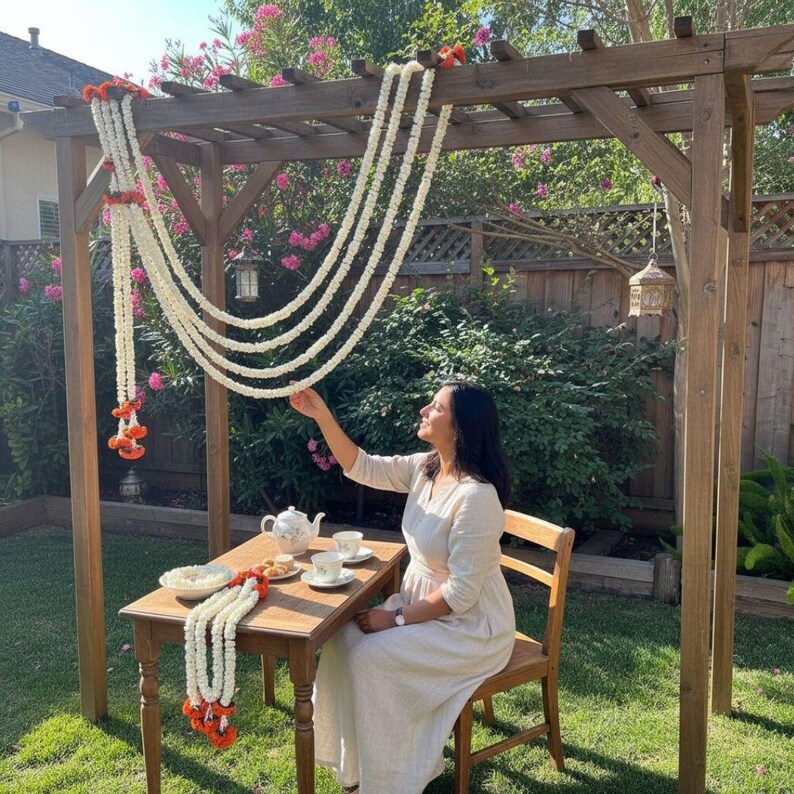 Woman in a garden setting with a decorated wooden pergola and table.