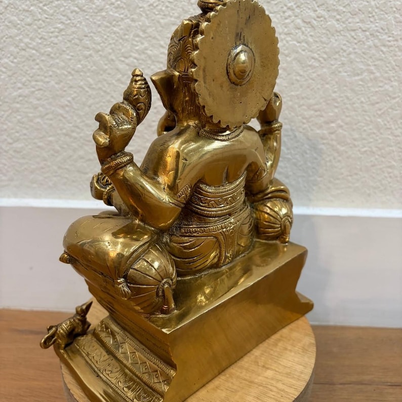 Back view of 9.5" Brass Ganesha on wooden base against textured wall — traditional Ganpati decor accent
