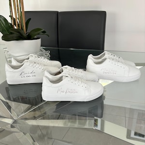 May include: Three pairs of white canvas sneakers with pink lettering. The sneakers are personalized with the words "Bride 15.06.26", "Mrs. Patterson", and "Mr. & Mrs. 24.07.24".