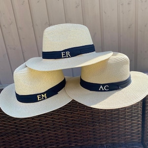 May include: Three straw hats with black bands and gold initials. The initials are "ER", "EM", and "AC".