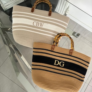 May include: Two striped tote bags with bamboo handles. The top bag is beige and white with the initials "CBW" embroidered on the front. The bottom bag is beige and black with the initials "DG" embroidered on the front.