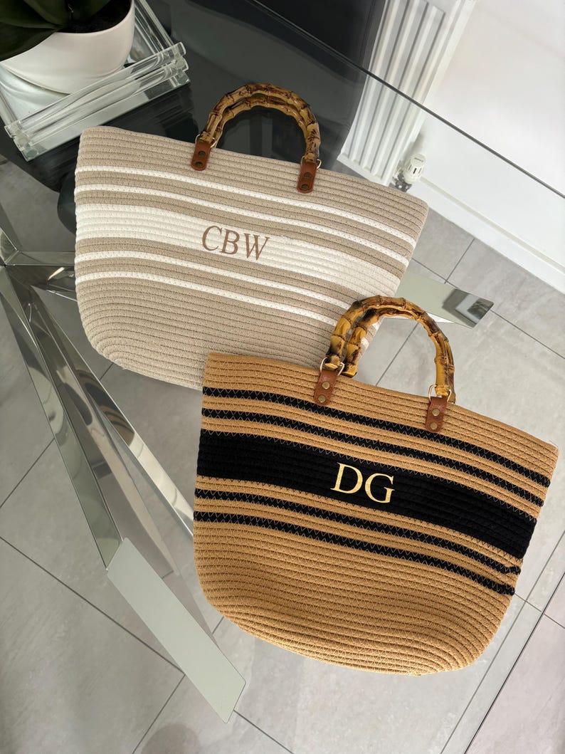 May include: Two striped tote bags with bamboo handles. The top bag is beige and white with the initials "CBW" embroidered on the front. The bottom bag is beige and black with the initials "DG" embroidered on the front.