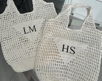 May include: Two white crocheted tote bags with black embroidered initials. The bag on the left has the initials "LM" and the bag on the right has the initials "HS".
